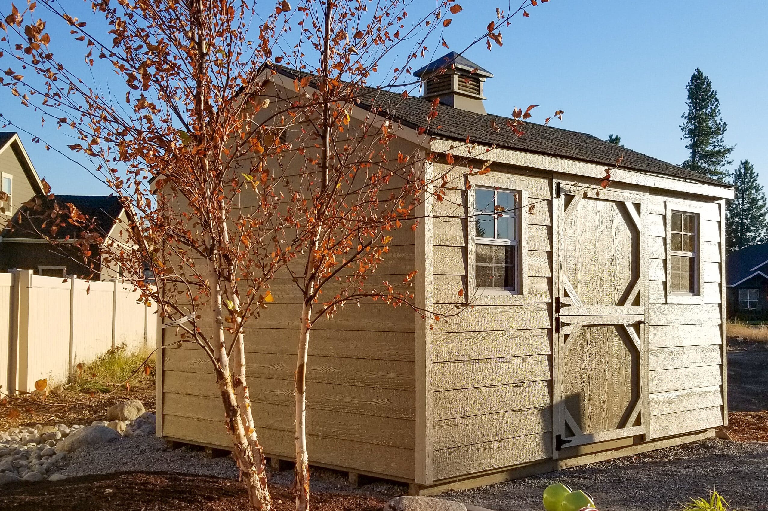 brown a frame shed with shingle roofing and cupola beside two trees with red leaves