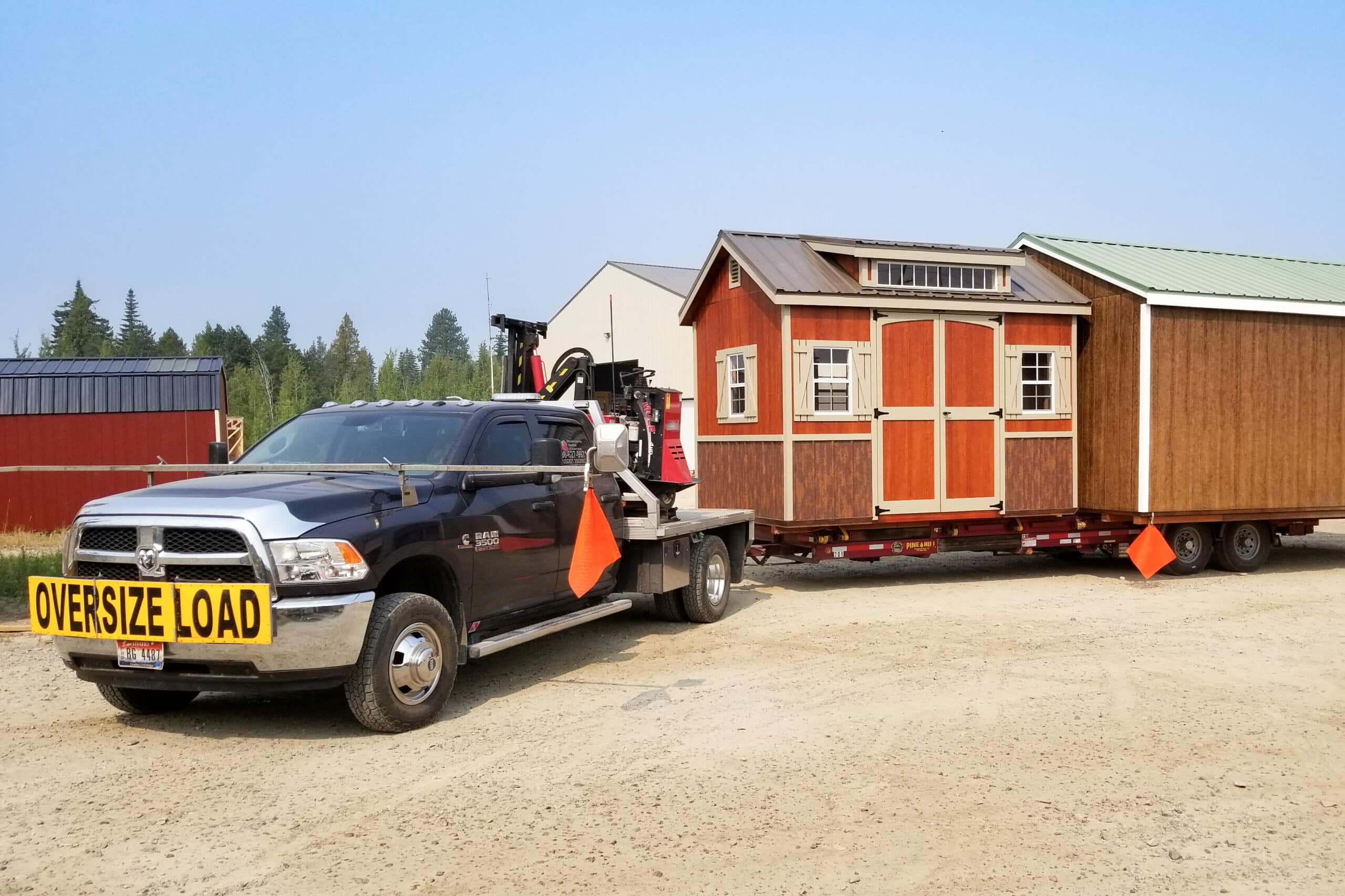 red and brown shed on back of trailer being pulled by black truck getting ready to delivered at sales lot in Surrey ND