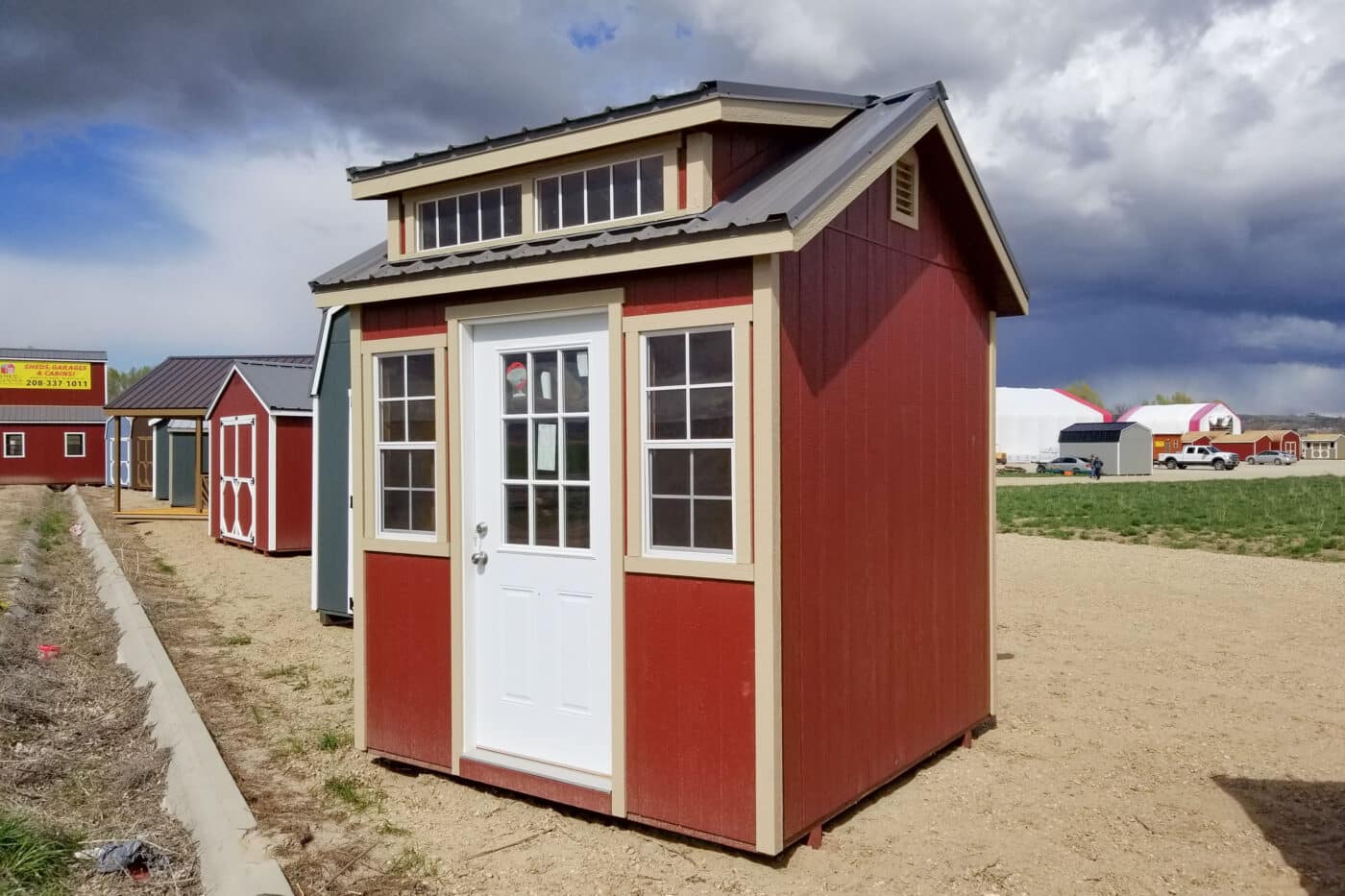 small red high shed with two windows and dormer and black metal roof and tan siding