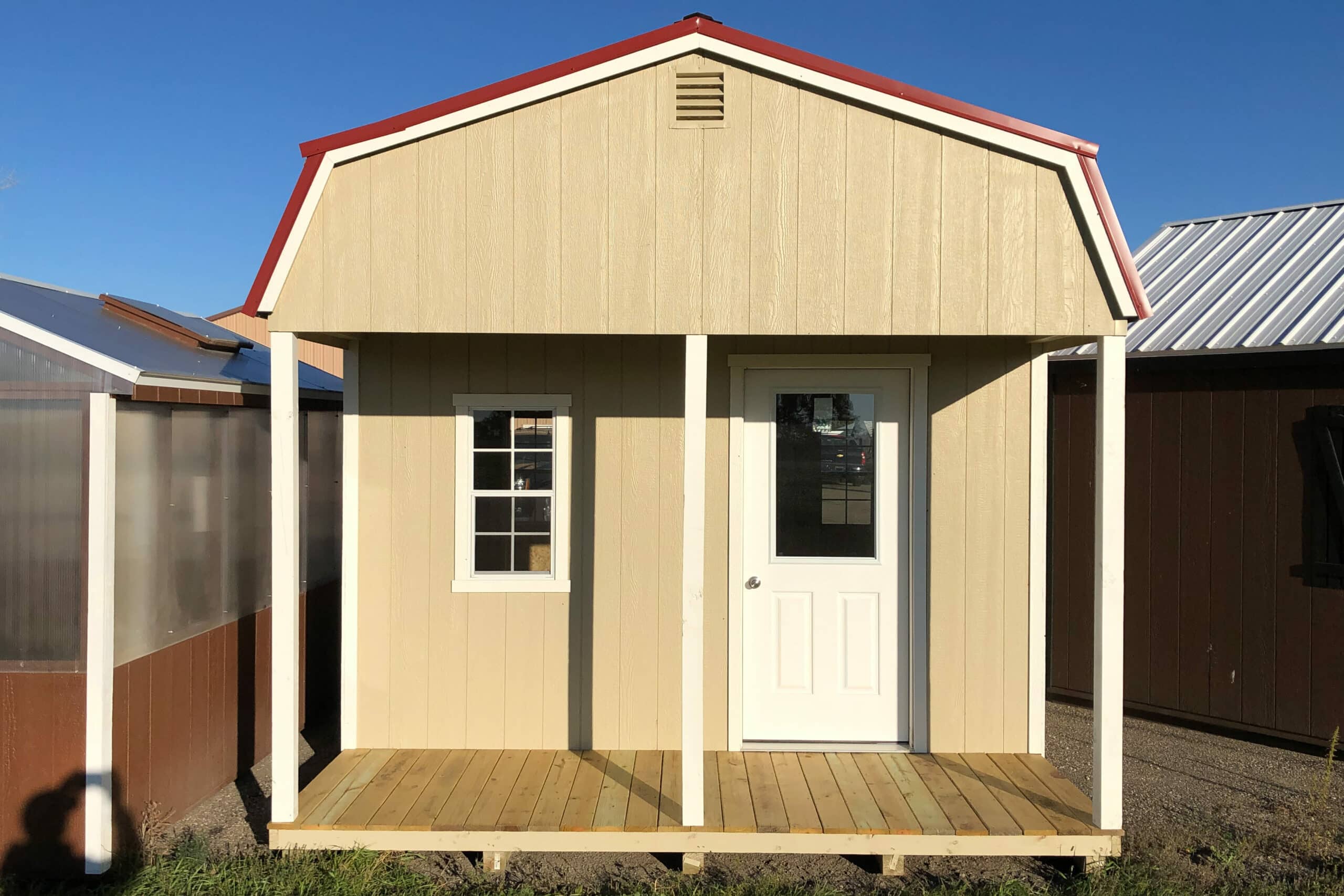 tan tiny cabin shed with red roof and white trim with wooden front porch and white front door in Surrey ND