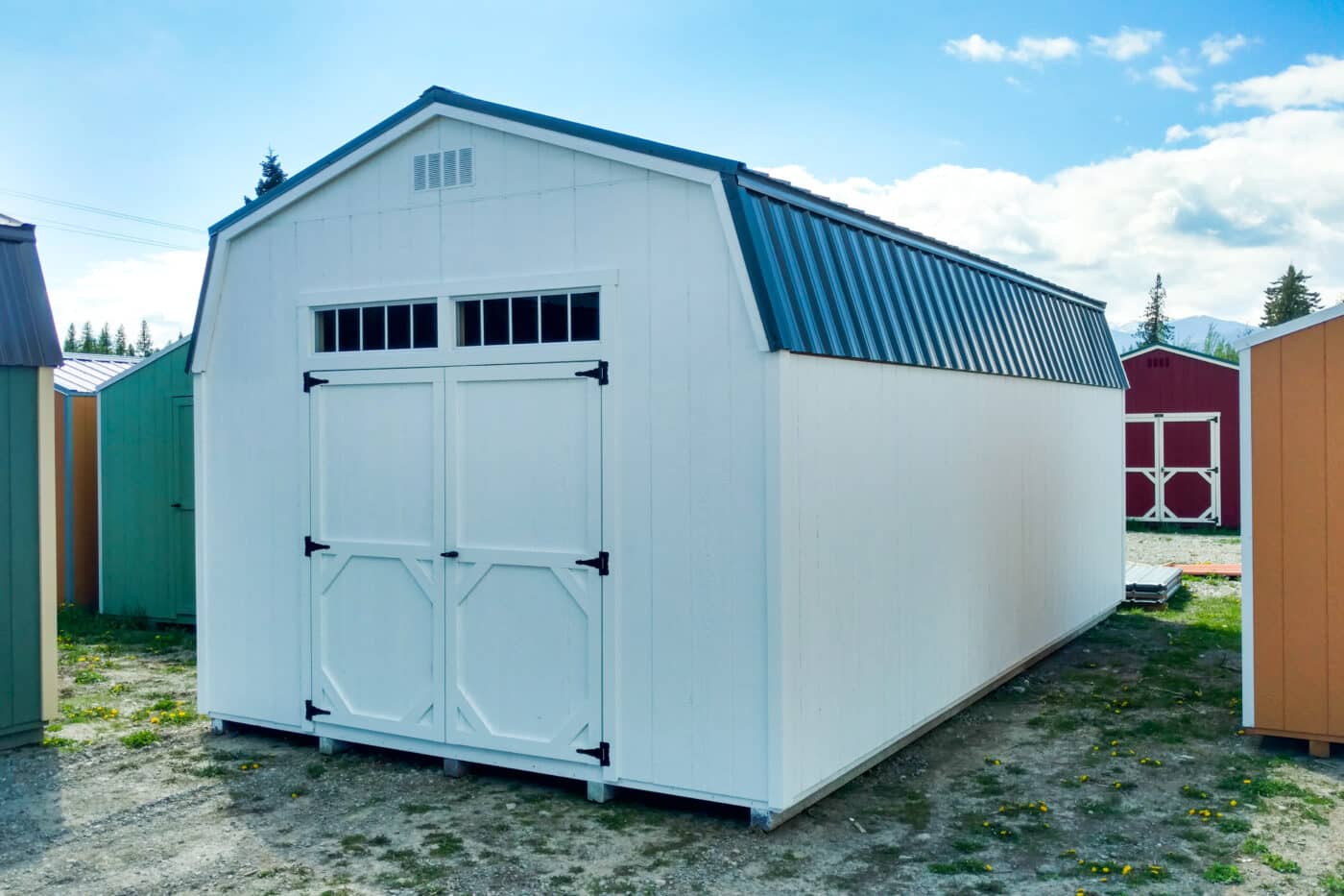 white gambrel shed with blue metal roof transom windows and a vent in compliance built with shed permit in Oregon